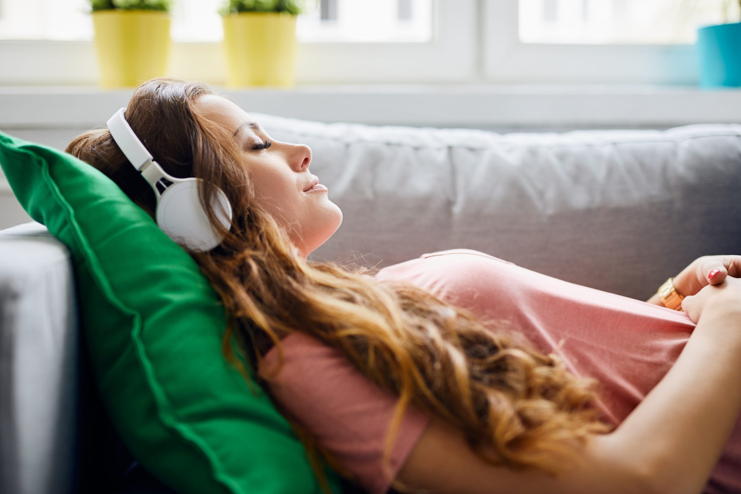 Portrait of a beautiful young woman lying on sofa with headphones on and closed eyes, relaxing Portrait of a beautiful young woman lying on sofa with headphones on and closed eyes, relaxing