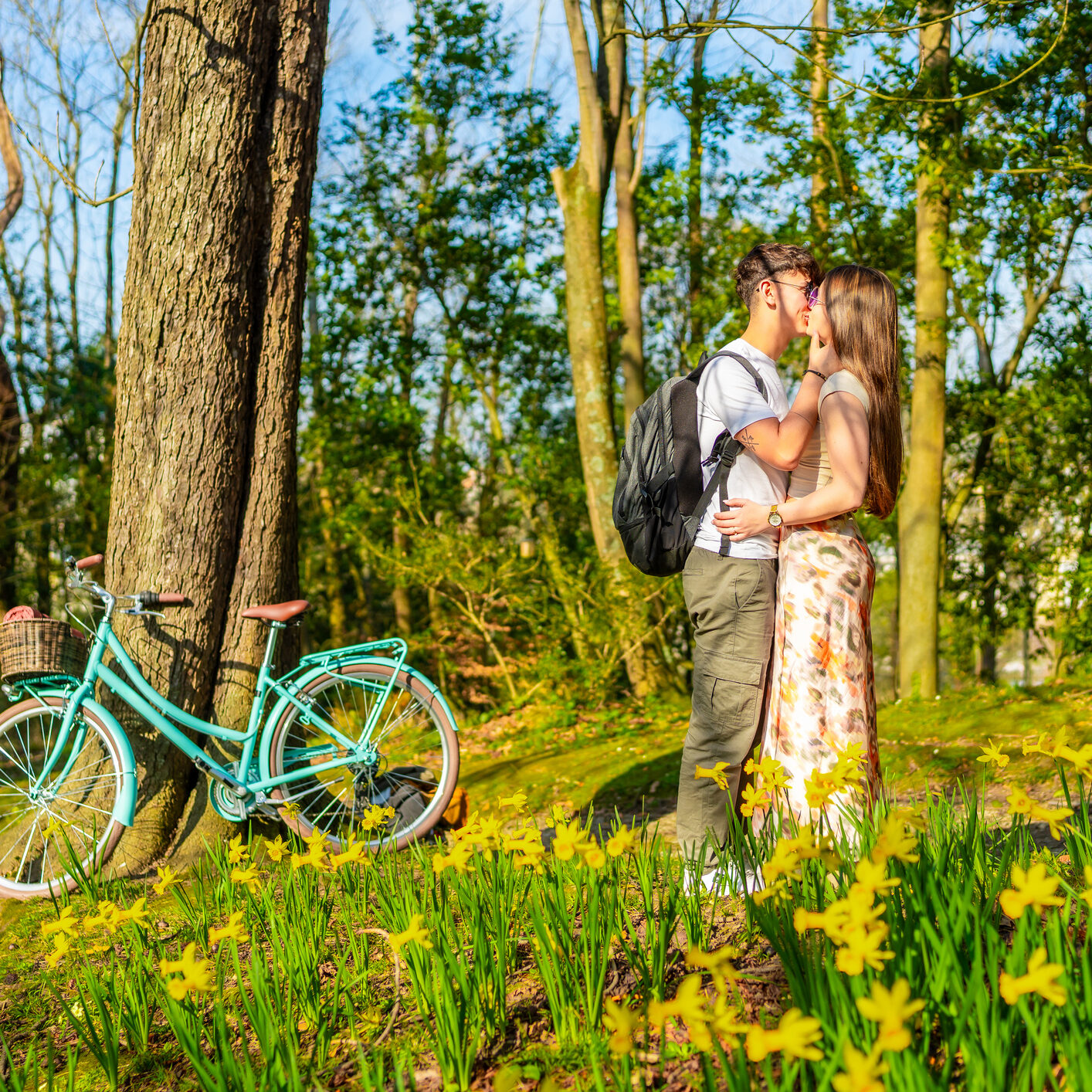 Young couple kissing in a field of daffodils with bicycle Young couple sharing a tender kiss amidst a vibrant spring forest, surrounded by blooming daffodils and a bicycle resting against a tree